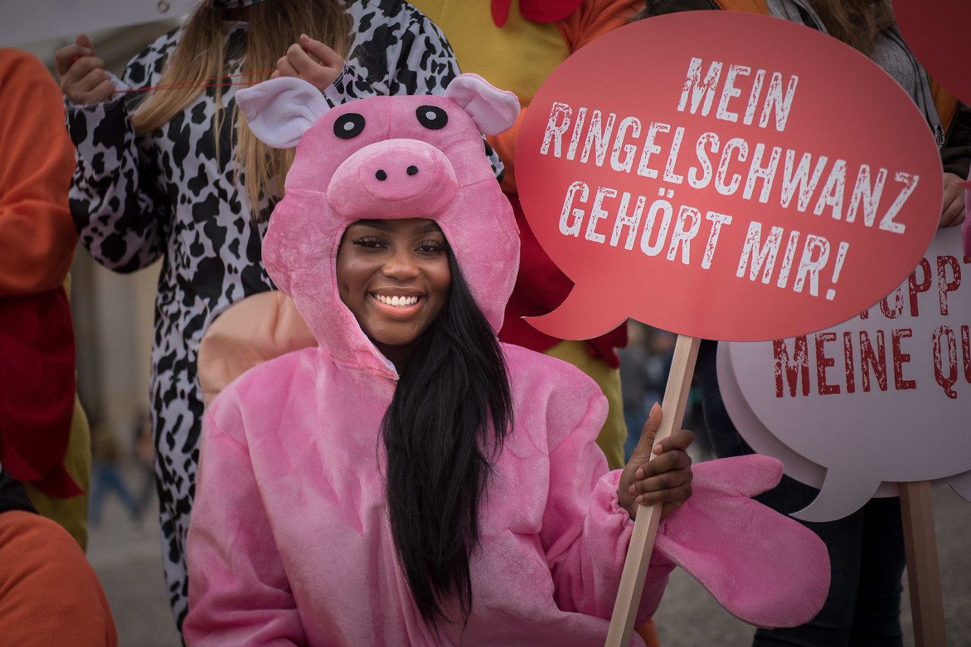 Eine Campact-Unterstützerin protestiert im Schweinskostüm gegen das Tierwohllabel. Sie hält ein Schild mit der Aufschrift "Mein Ringelschwanz gehört mir"."