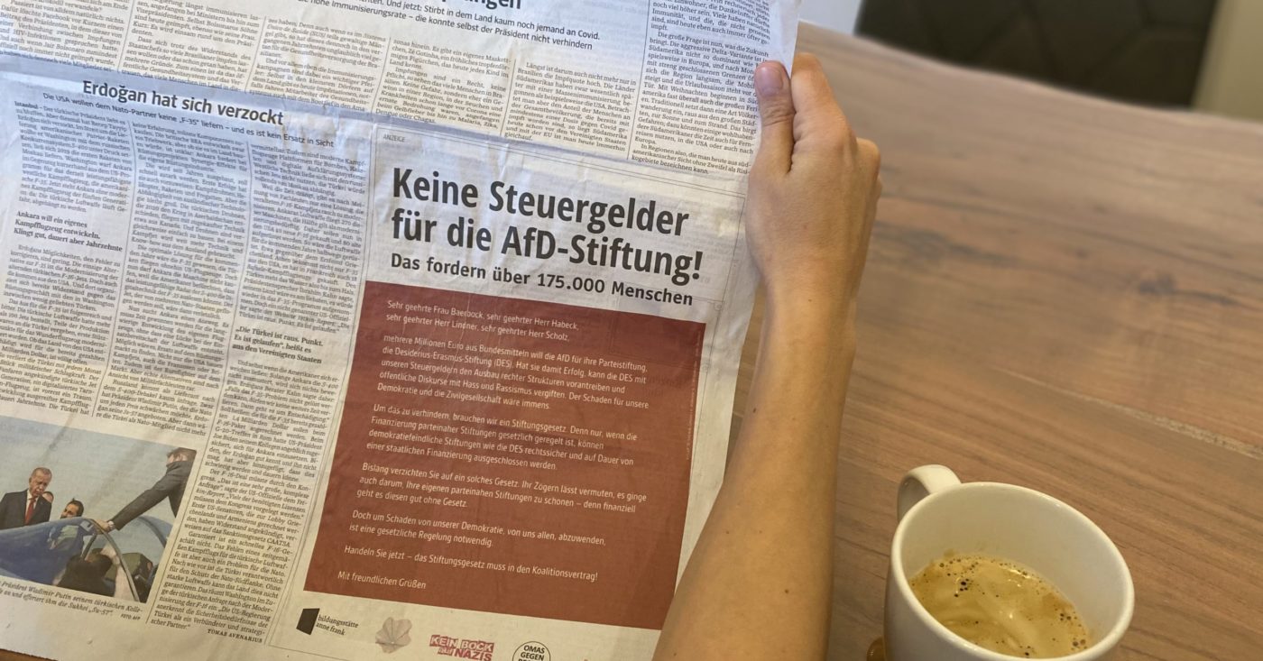 Eine Hand hält eine Zeitung in der die Anzeige "Keine Steuergelder für die AfD-Stiftung!" abgedruckt ist.