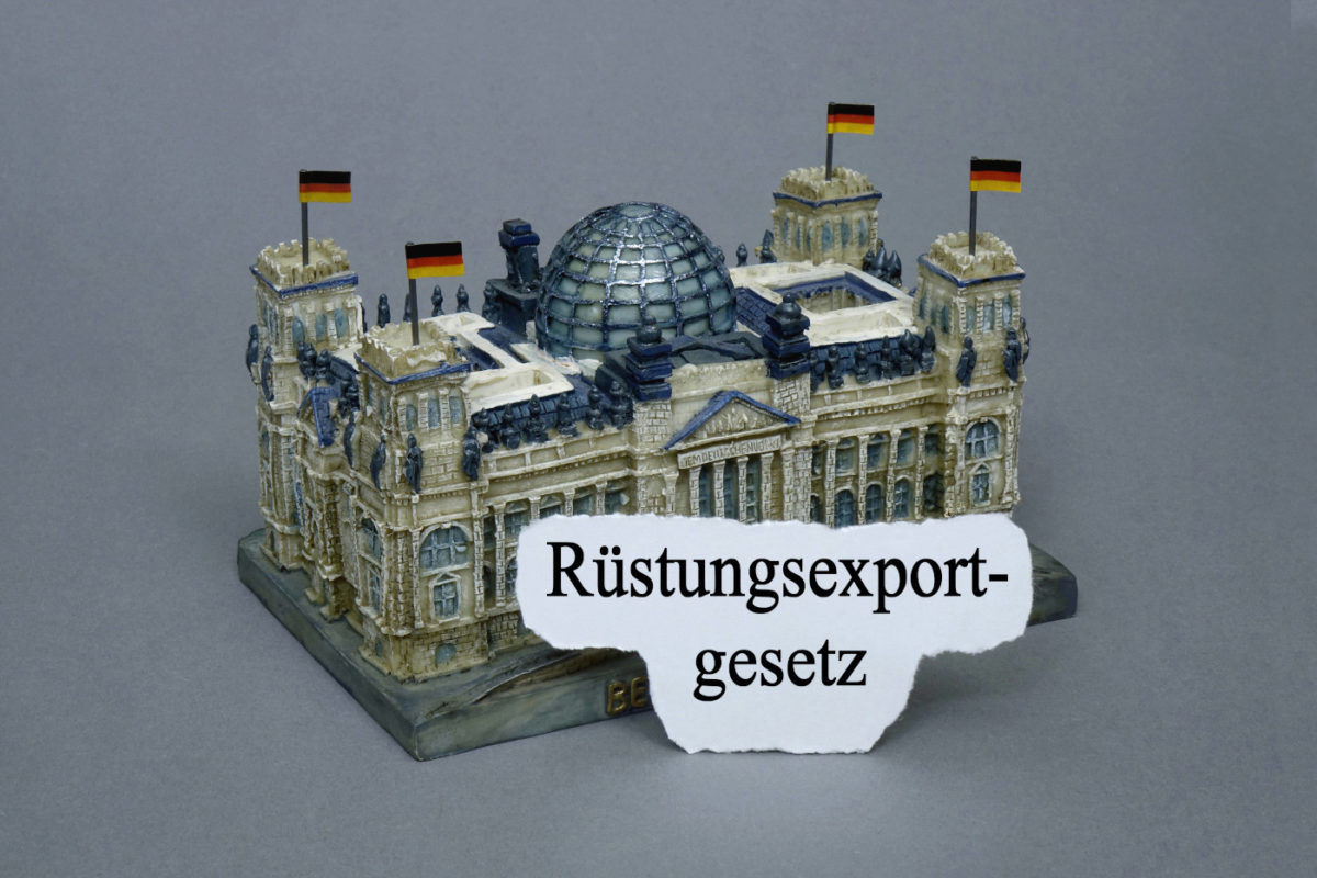 Das Foto zeigt eine Miniatur des Reichstagsgebäudes. Daran gelehnt steht ein Stück Papier mit dem Schriftzug: Rüstungsexport-gesetz.