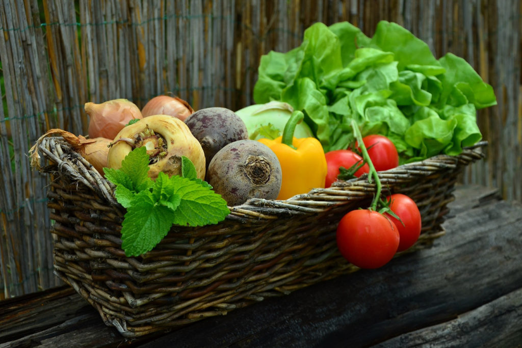 Das Foto zeigt einen Weidenkorb, in dem verschiedene Gemüsesorten liegen, zum Beispiel ein großer Salatkopf, Paprika, Tomaten, Rote Beete und Zwiebeln. 