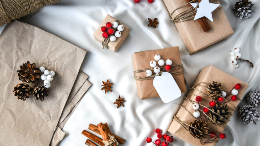 Das Foto zeigt verschieden eingepackte kleine Geschenke auf einem weißen Untergrund. Die Päckchen sind in braunes Papier eingepackt und mit Zweigen und Tannenzapfen verziert.