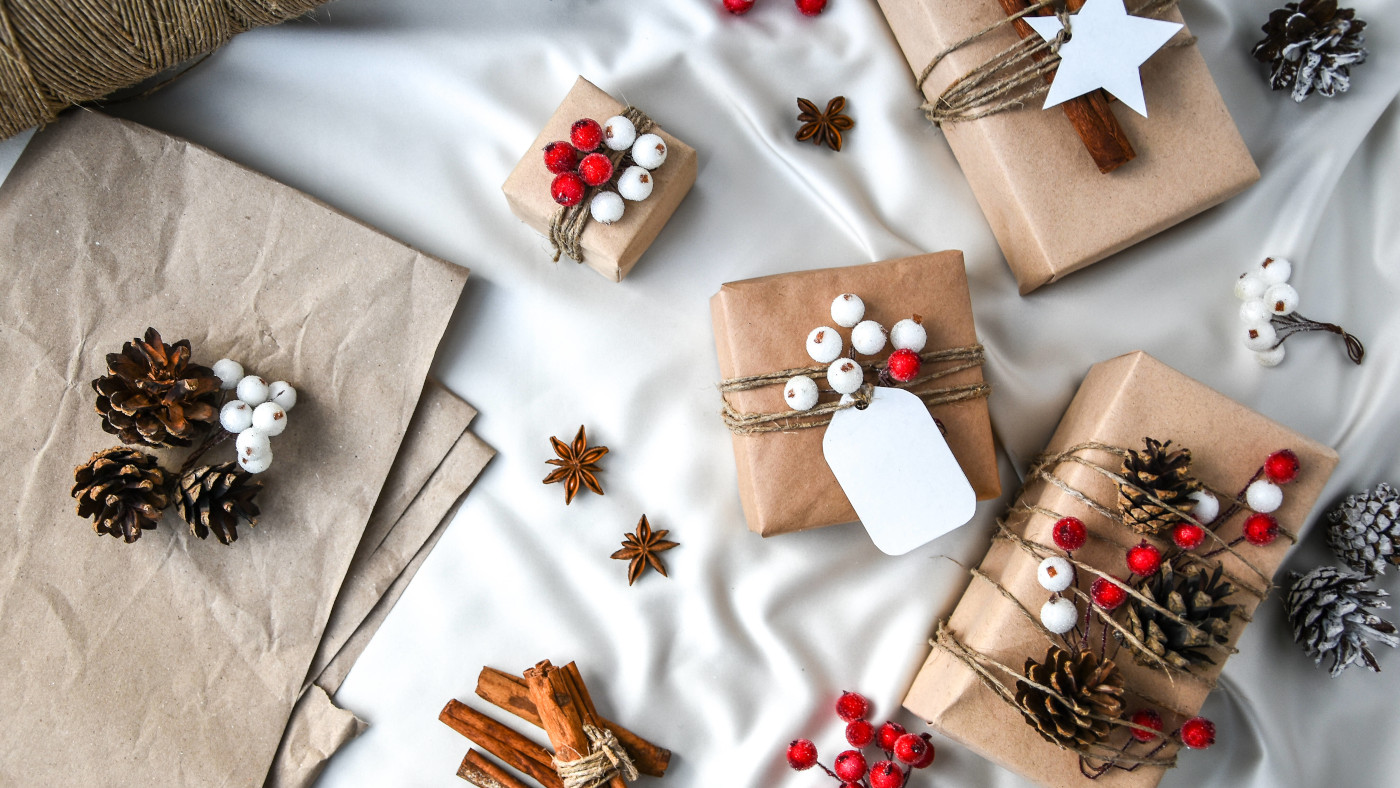 Das Foto zeigt verschieden eingepackte kleine Geschenke auf einem weißen Untergrund. Die Päckchen sind in braunes Papier eingepackt und mit Zweigen und Tannenzapfen verziert.