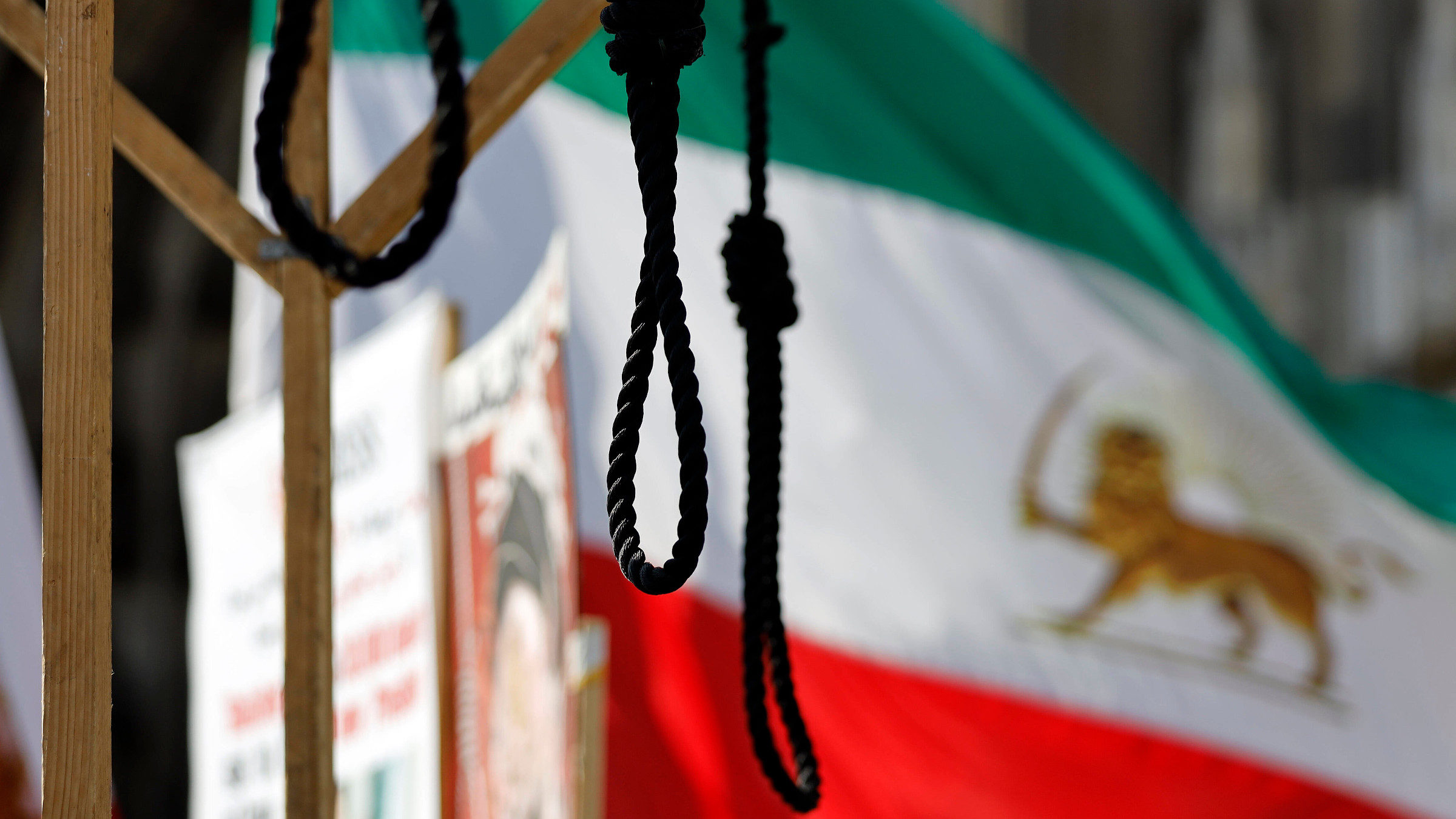 Ein Strick hängt an einem Galgen, im Hintergrund ist eine iranische Flagge zu sehen. Das Bild wurde bei einer Demonstration von Iraner*innen in Berlin aufgenommen.