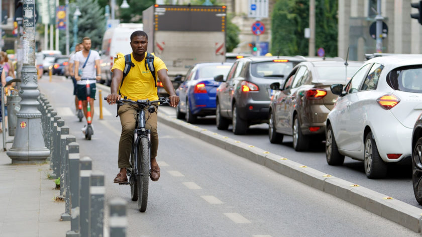 Ein Mann fährt auf einem Fahrrad durch die Stadt. Die Autos auf der entgegenkommenden Fahrbahn stehen im Stau.