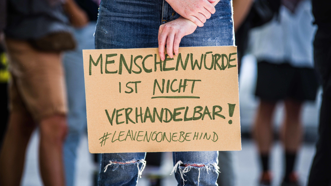 "Menschenwürde ist nicht verhandelbar!" steht auf einem Schild aus Pappe, das eine Person vor sich in der Hand hält.