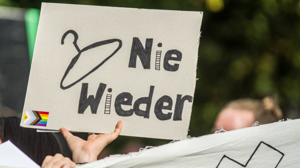 Ein Foto von einer Demo für die Legalisierung von Schwangerschaftsabbrüchen – darauf zu sehen ist ein Plakat mit einem Kleiderbügel und der Aufschrift "Nie wieder"