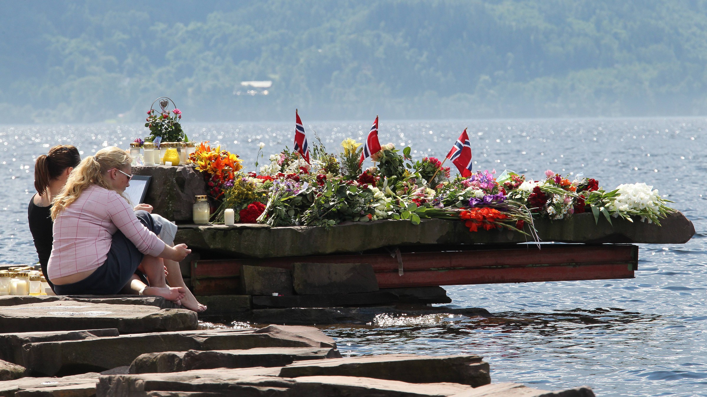 Zwei Personen sitzen am Wasser und trauern um die Opfer des rechtsextremistischenAnschlags auf Utøya.