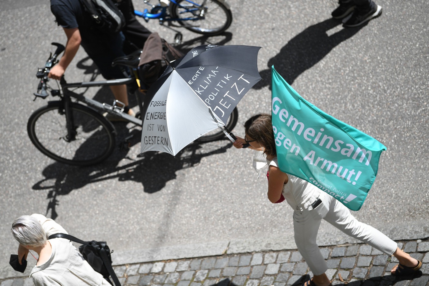 Eine Aufnahme bei der G7-Demo 2022: Eine Frau hält einen Regenschirm mit der Aufschrift "Echte Klimapolitik jetzt!" und eine Campact-Flagge, auf der steht "Gemeinsam gegen Armut"