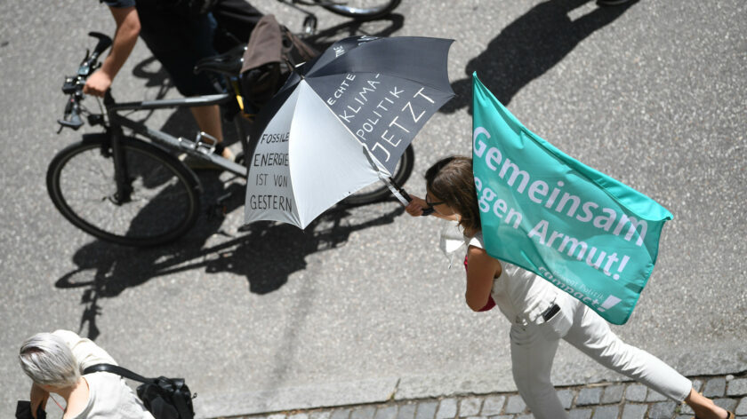 Eine Aufnahme bei der G7-Demo 2022: Eine Frau hält einen Regenschirm mit der Aufschrift "Echte Klimapolitik jetzt!" und eine Campact-Flagge, auf der steht "Gemeinsam gegen Armut"