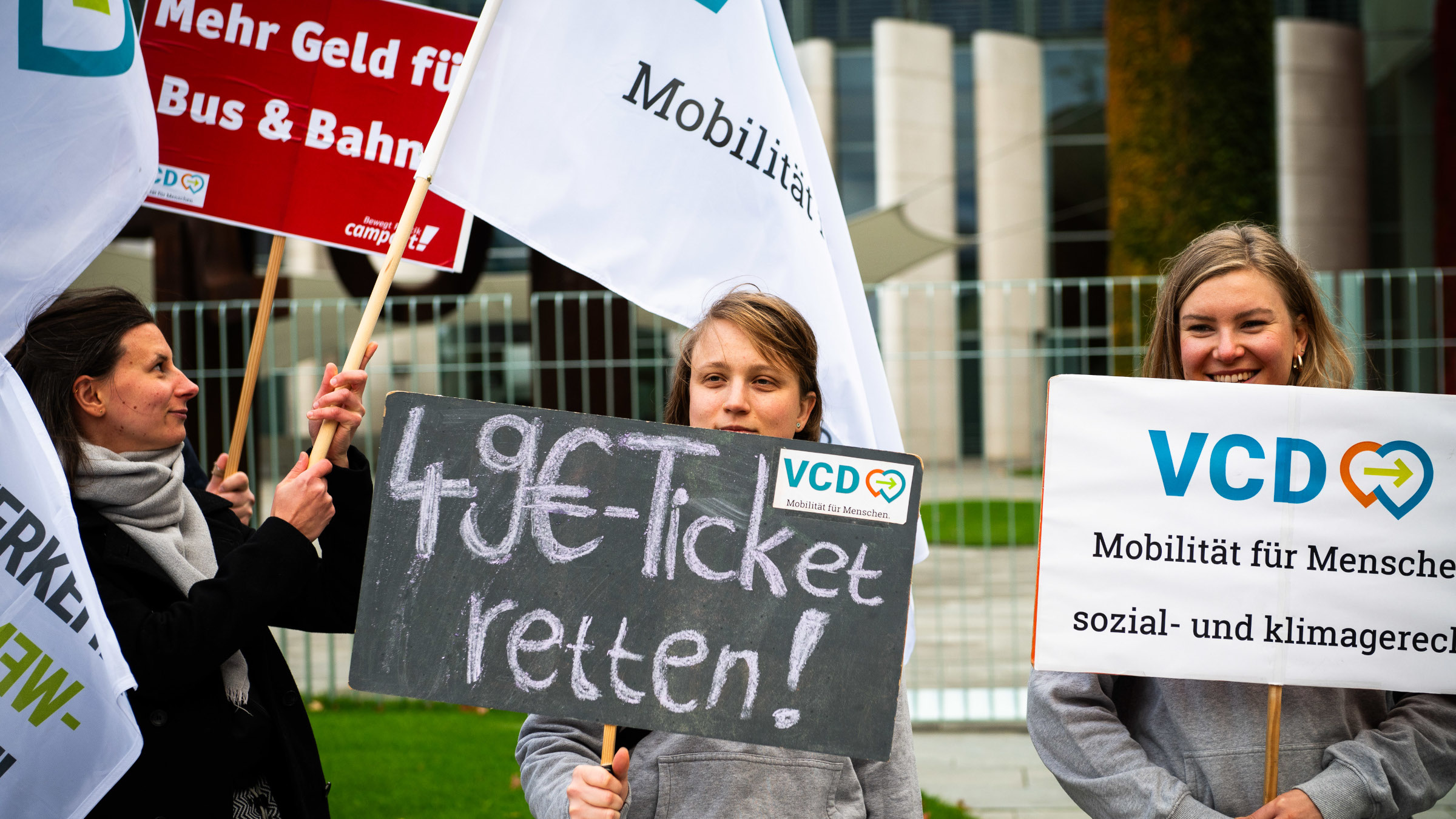 Zu sehen sind drei Frauen, die verschiedene Protest-Schilder hochhalten. Auf ihnen steht: "Mehr Geld für Bus und Bahn!", "49€-Ticket retten" Das Foto ist entstanden bei einer Demo zum Deutschlandticket im Oktober 2023.