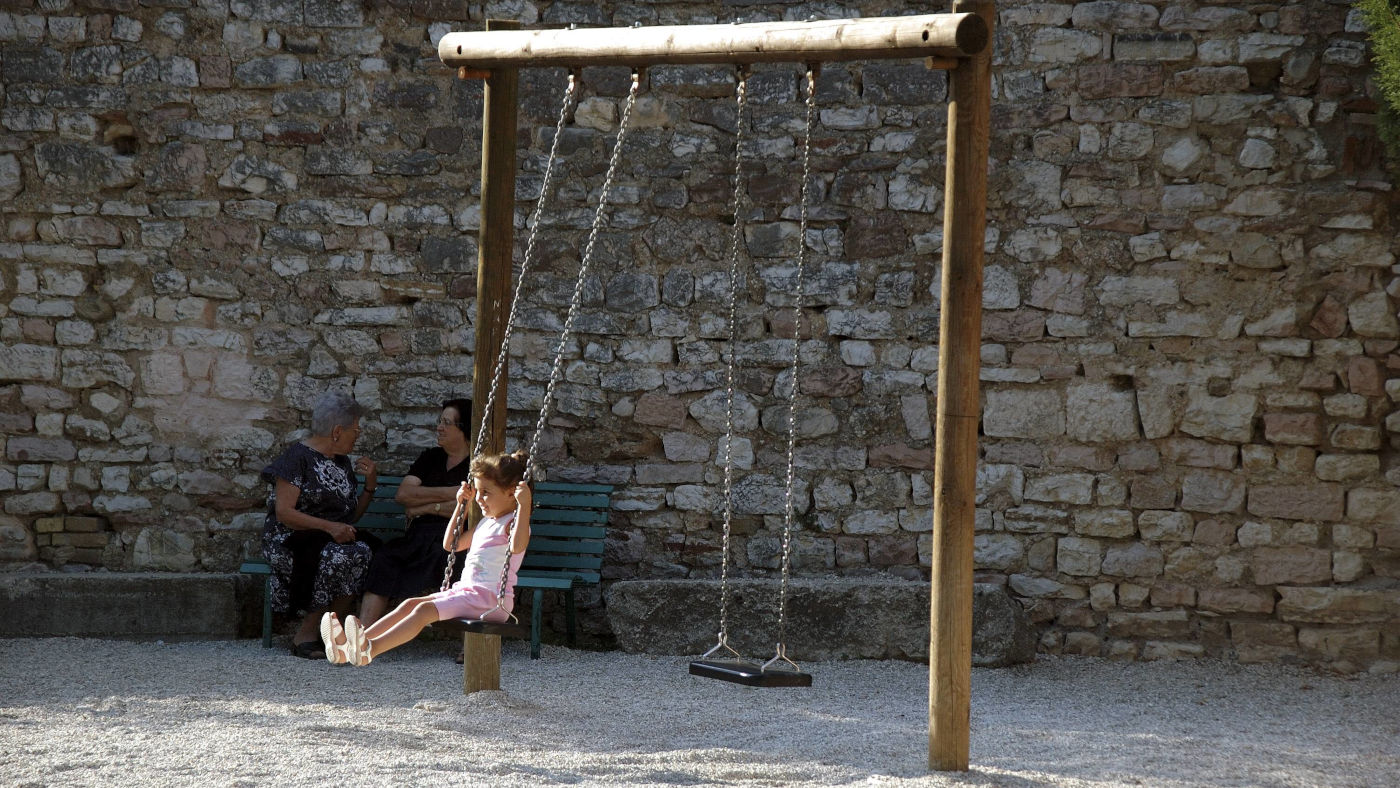 Ein Kind auf einer Schaukel und zwei älterer Frauen auf einem Spielplatz in Assisi, Italien.