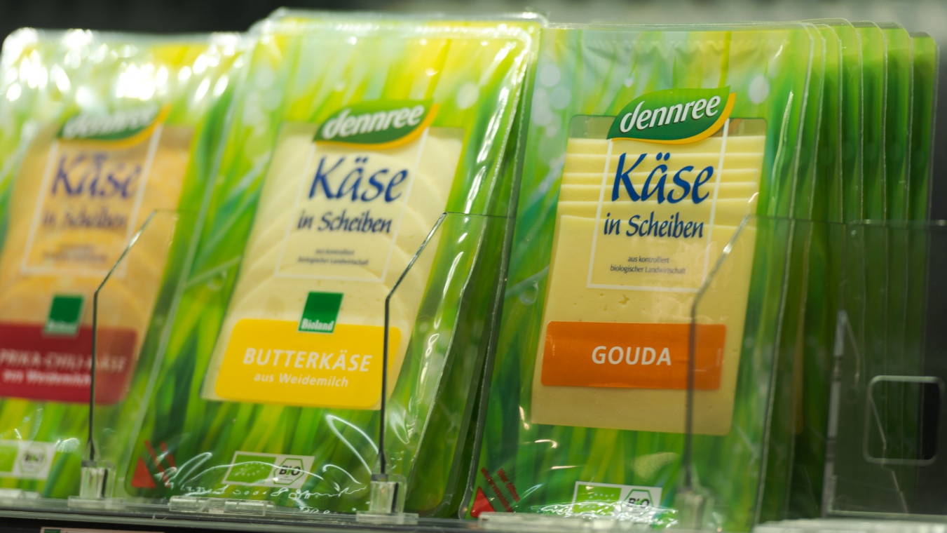 Ein Supermarkt-Kühlregal, in dem mehrere unterschiedliche Sorten Käsescheiben der Marke Dennree abgepackt hintereinander stehen.