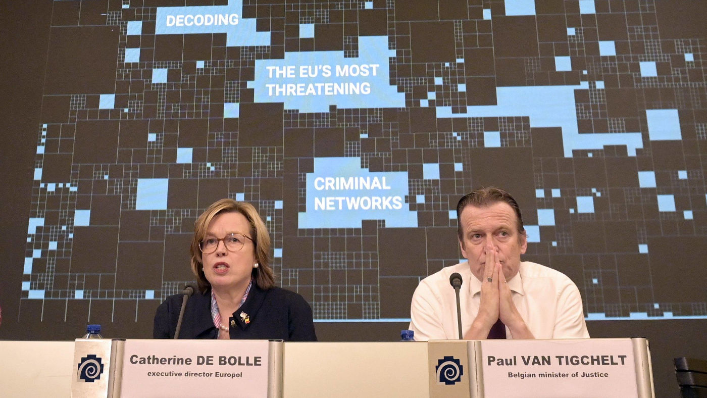 Europol-Chefin Catherine De Bolle (links) und der Justizminister von Belgien Paul Van Tigchelt (rechts) bei einer Pressekonferenz Anfang April. Hinter ihnen ist eine große Plakatwand zu sehen, auf der in pixeligen Buchstaben steht: "Decoding the EU's most threatening criminal networks".
