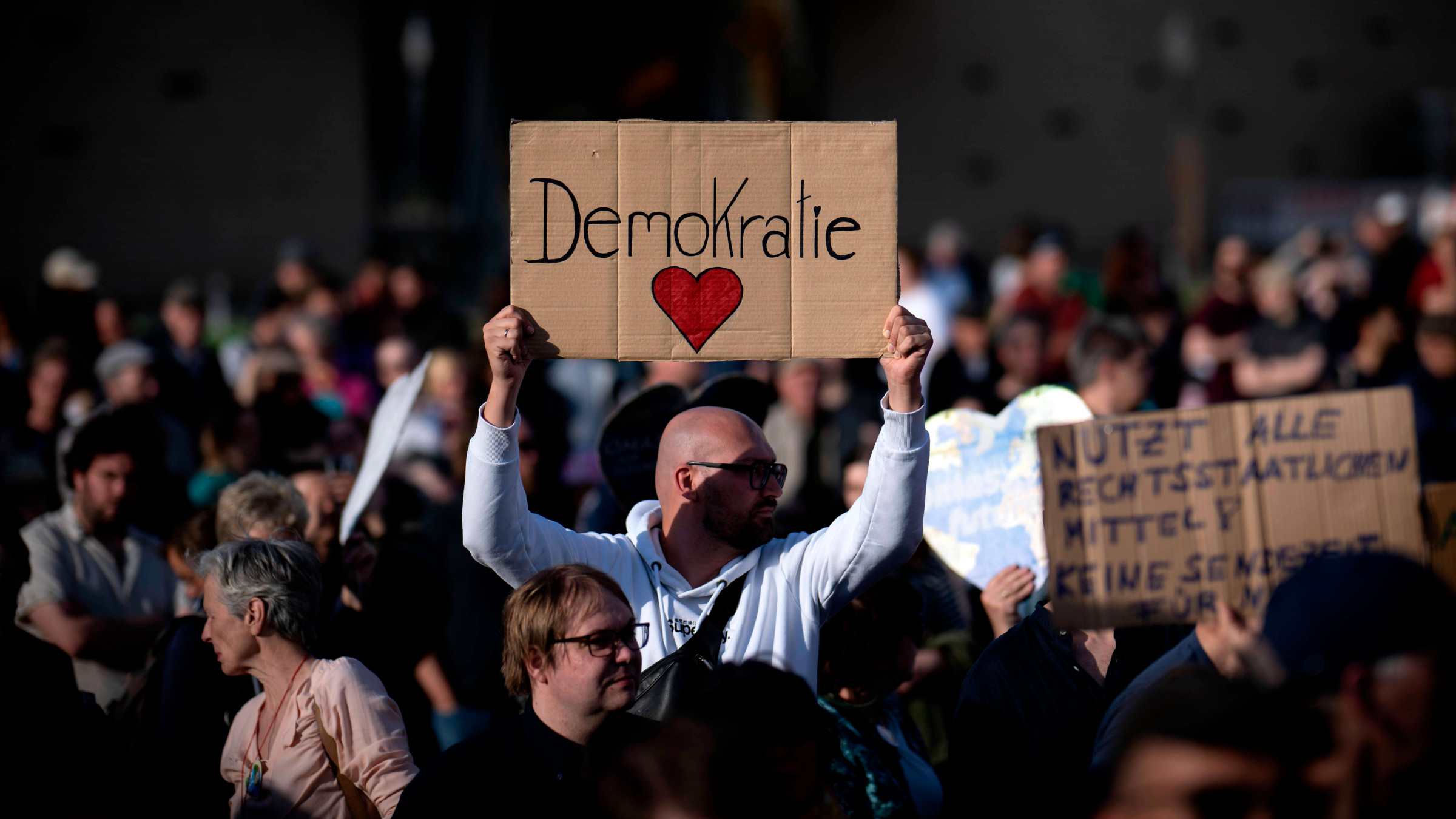 Bei einer Demo gegen rechte Gewalt in Berlin hält eine Person ein Schild hoch, auf dem die Aufschrift"Demokratie" und ein rotes Herz zu sehen sind.