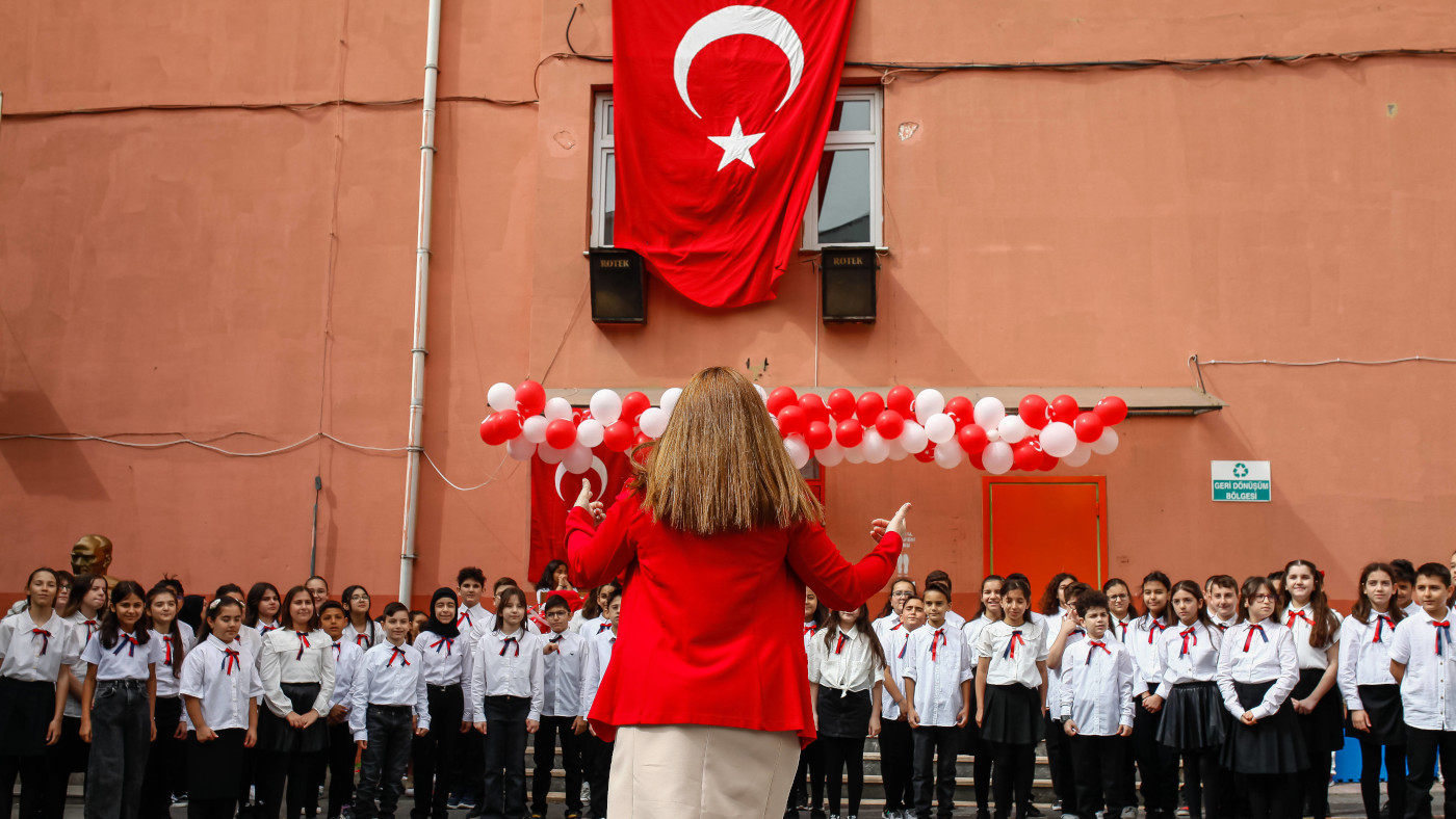 Eine Lehrerin in einem roten Blazer steht mit dem Rücken zur Kamera. Sie dirigiert Schülerinnen und Schüler einer Grundschule in Istanbul.