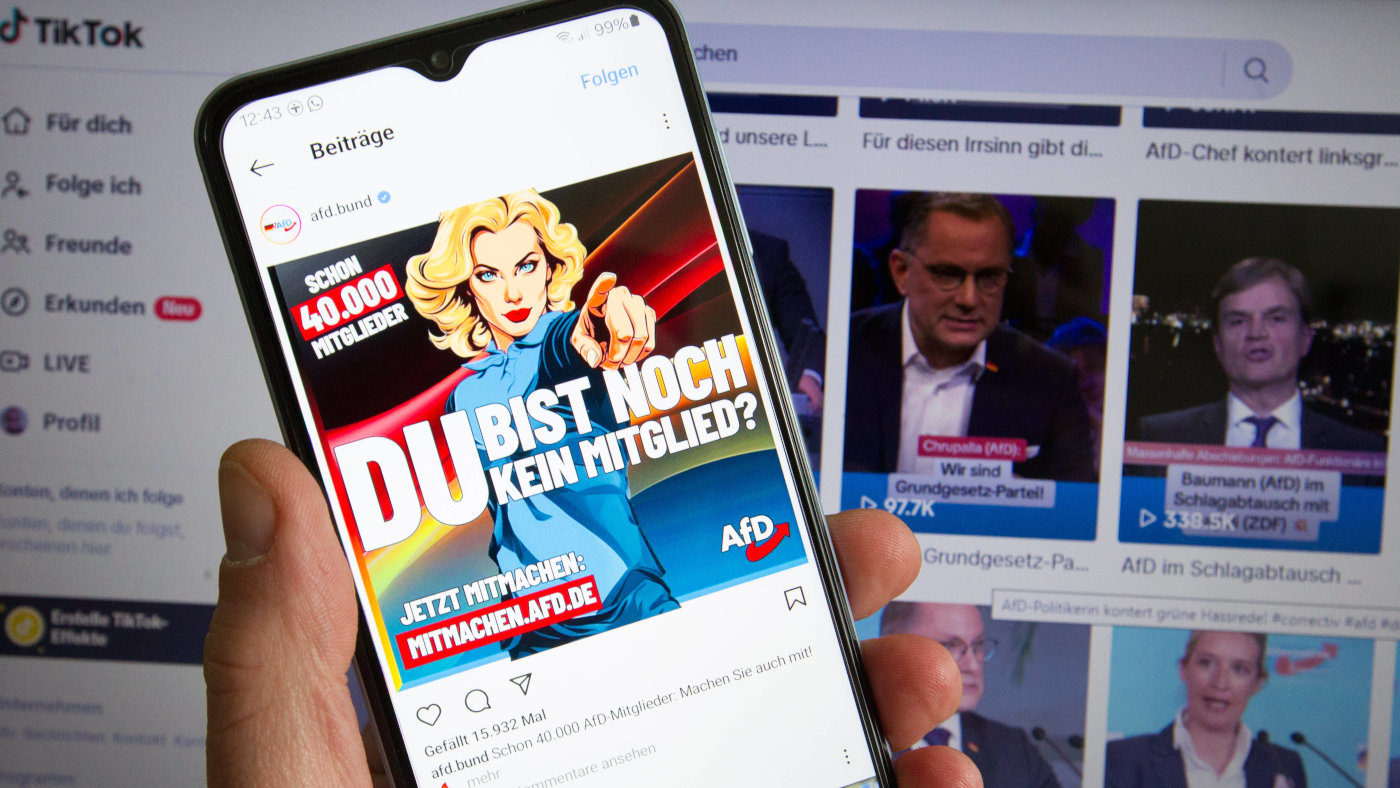 Ein Mann hält ein Smartphone in der Hand, auf dem der Instagram-Account der Partei Alternative für Deutschland geöffnet ist. Im Hintergrund ein Laptop mit dem Tiktok-Kanal der AfD.
