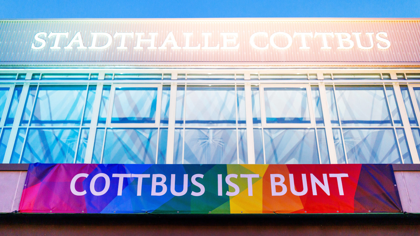 "Cottbus ist bunt" steht auf einem großen Transparent ins Regenbogenfarben, dass an der Stadthalle in Cottbus hängt.