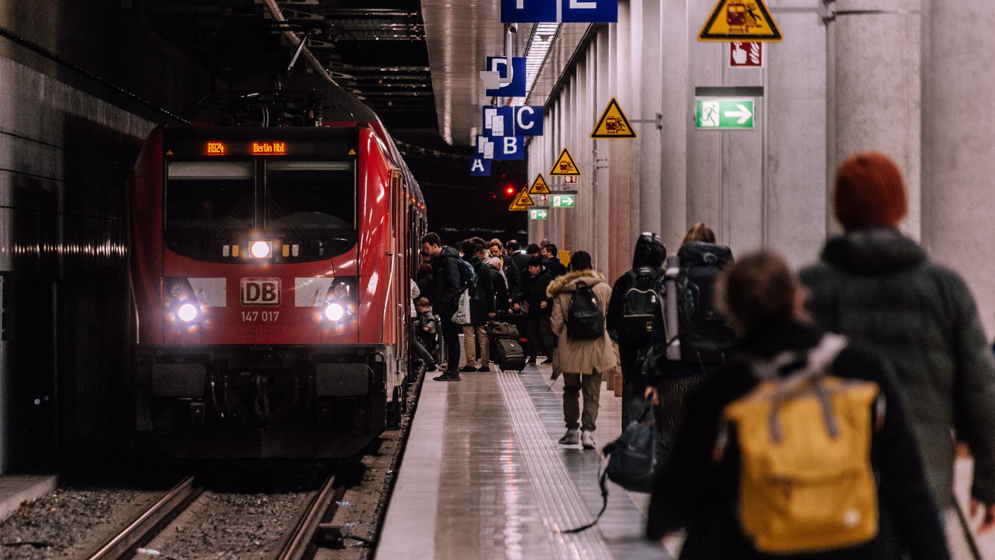 Ein Zug fährt in einen unterirdischen Bahnhof ein. Am Bahnsteig warten Reisende.