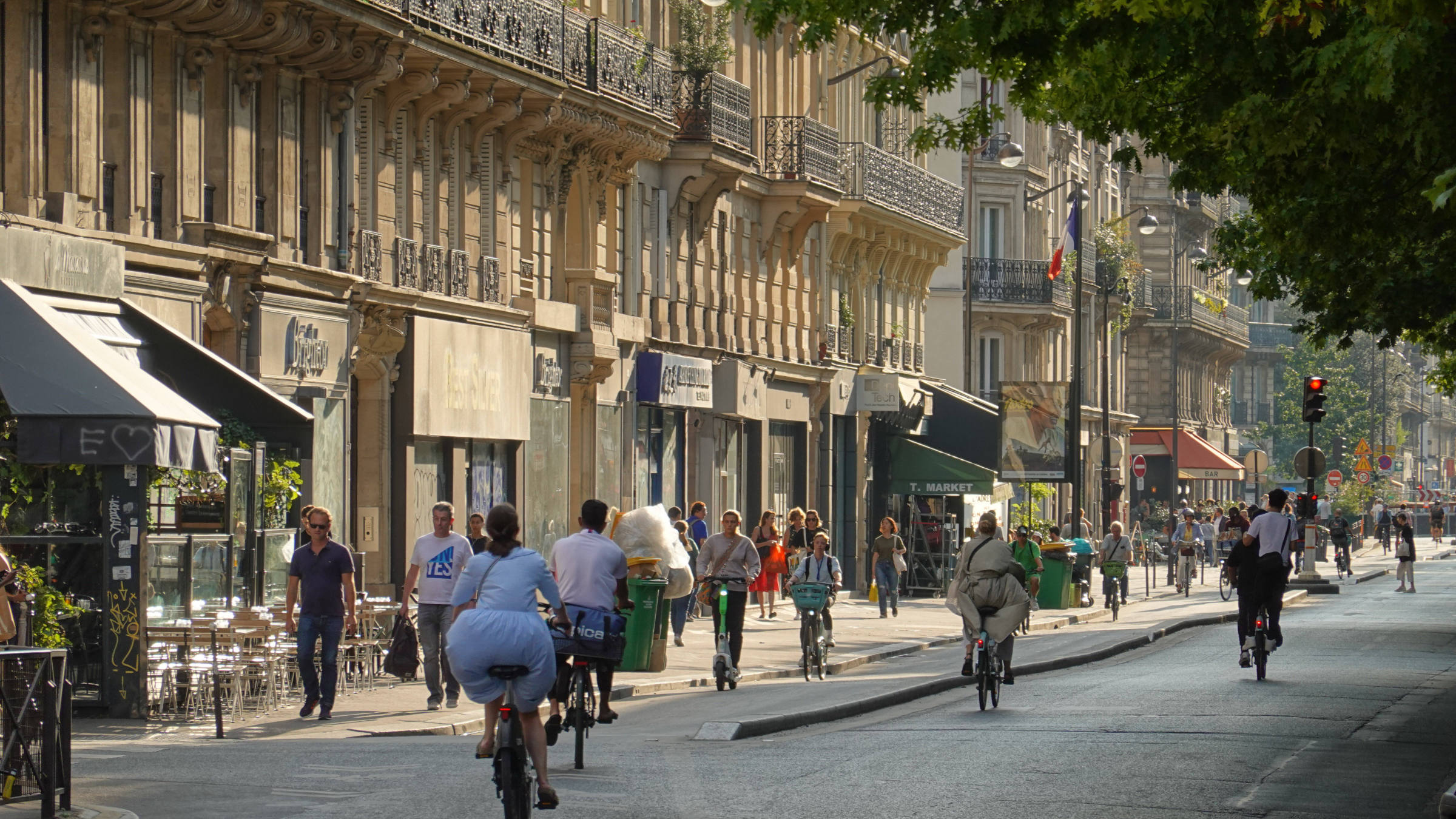 Ein belebte Straße in Paris mit viel Grün. Auf der Straße sind Fußgänger und Fahrradfahrer – keine Autos. Paris ist ein Postivbeispiel für eine gelungene Verkehrswende.