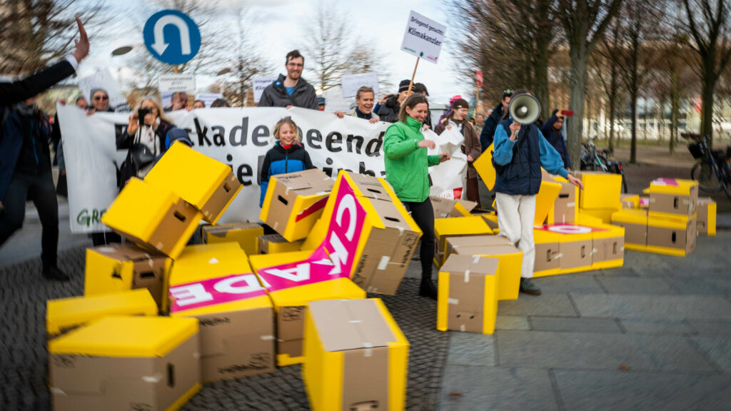 Campact protestiert gegen die Klimablockade der FDP. Dafür durchbrechen Menschen bei einer Demo symbolisch eine Mauer aus gelben Pappkartons.