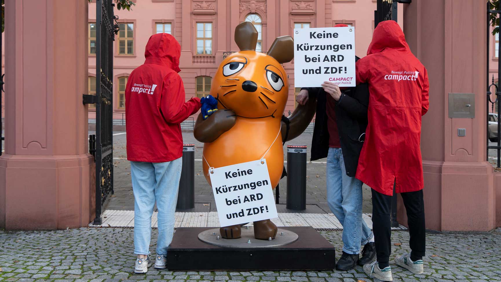 Die menschengroße Maus-Statue vor der Staatskanzlei in Mainz. Um ihren Hals hängt ein Schild mit der Forderung: "Keine Kürzungen bei ARD und ZDF!"