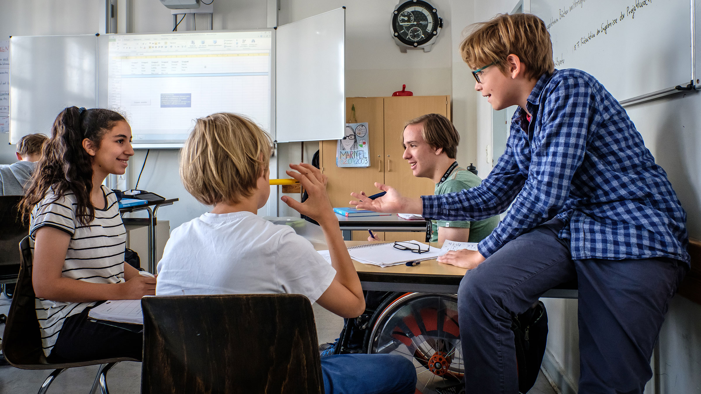 Vier Schüler in ihrem Klassenzimmer. Ein Schüler sitzt im Rollstuhl.