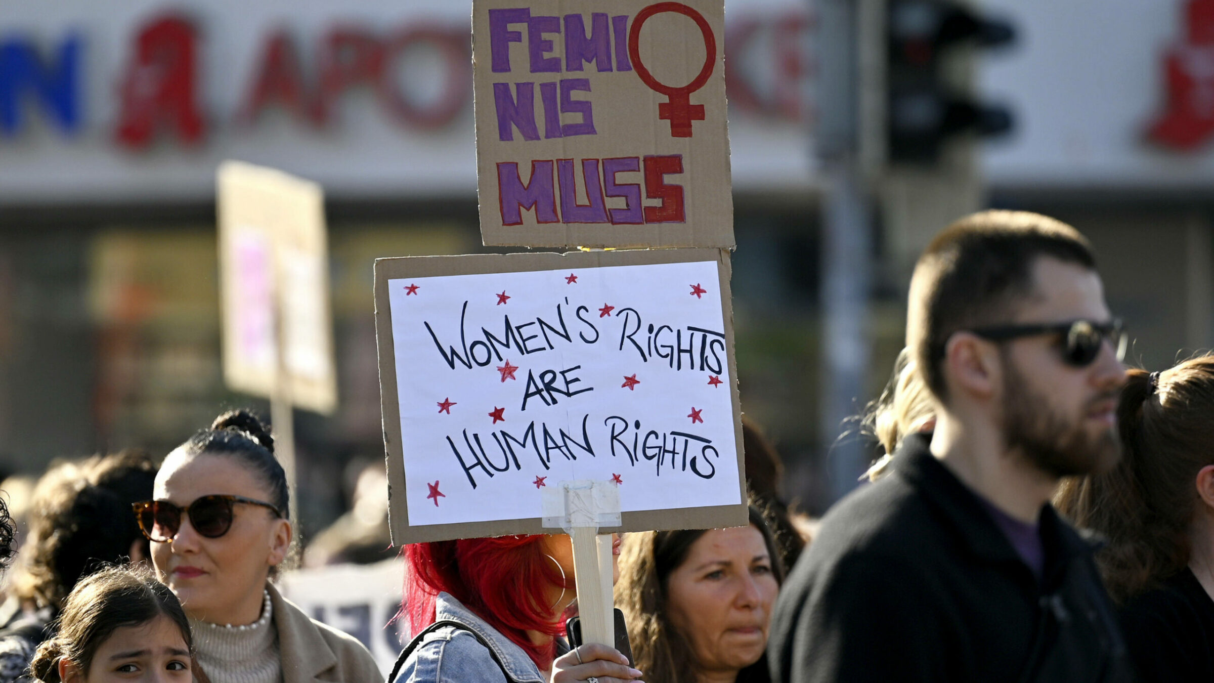 Demonstration für Frauenrechte und Gleichberechtigung, Menschen halten Schilder mit feministischen Botschaften beim Protest. Vordergrund zeigt Plakat mit "Women's Rights are Human Rights".